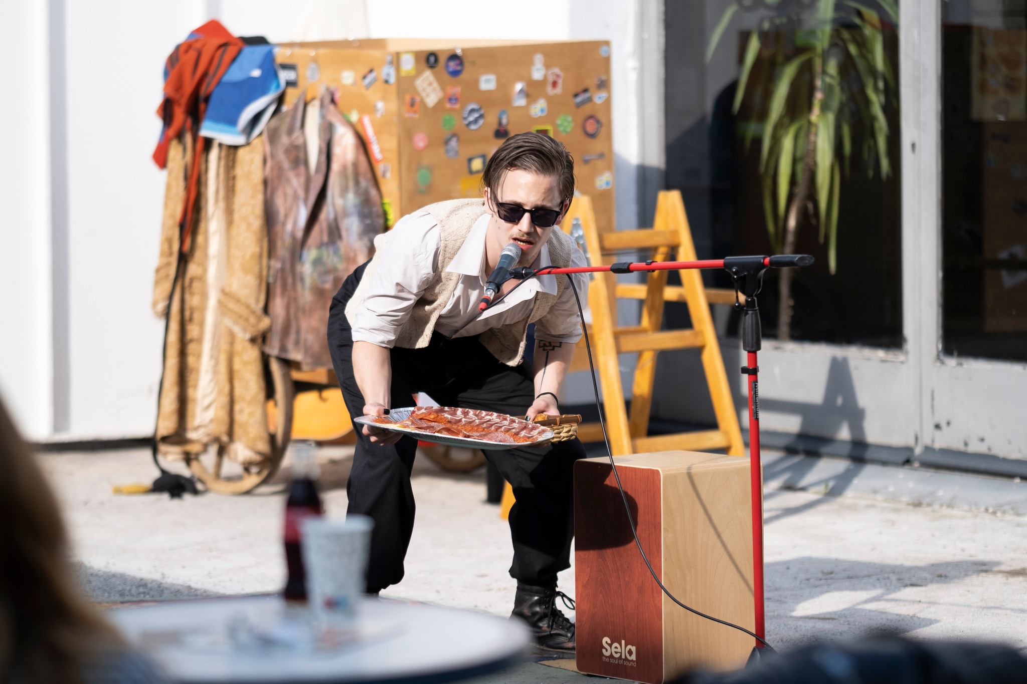 Fotografija prikazuje glumca koji drži pladanj s mesnim narescima i govori u mikrofon.