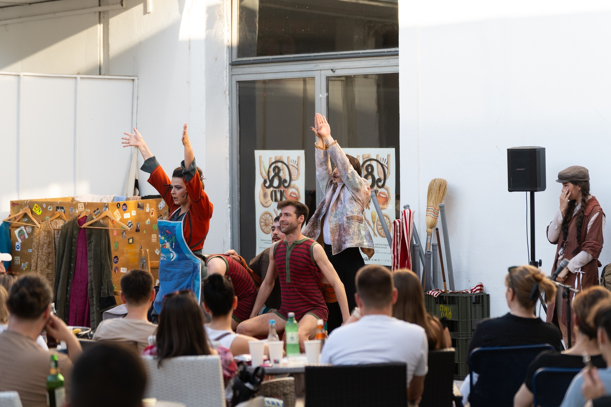 Fotografija prikazuje situaciju iz predstave. U eksterijeru atrija &TD-a nalazise petero glumaca koji igraju prema publici, te još jedna glumica koja se u pozadini smije njihovoj igri.