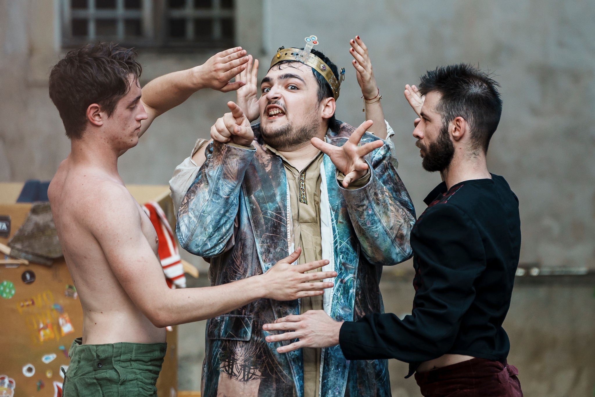 Fotografija prikazuje glumca koji igra Kralja Ubuja u grimasi, kako pruža ruke zgrčenih prstiju prema objektivu, dok s njegove lijeve i desne strane stoje dva glumca neutralnih izraza lica, a iza njega se nazire još jedan par ruku čijeg vlasnika ili vlasnicu ne vidimo.